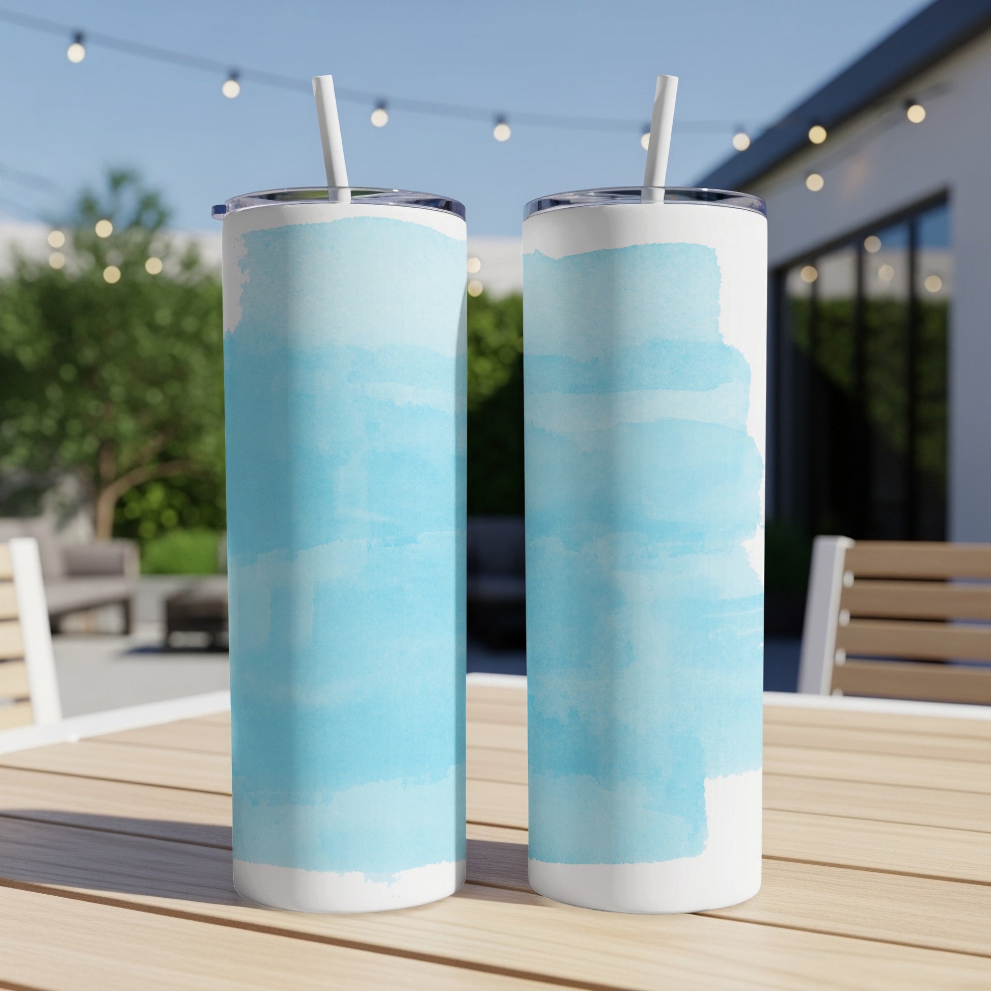 Two blue watercolor-splattered tumblers with straws on a wooden table.
