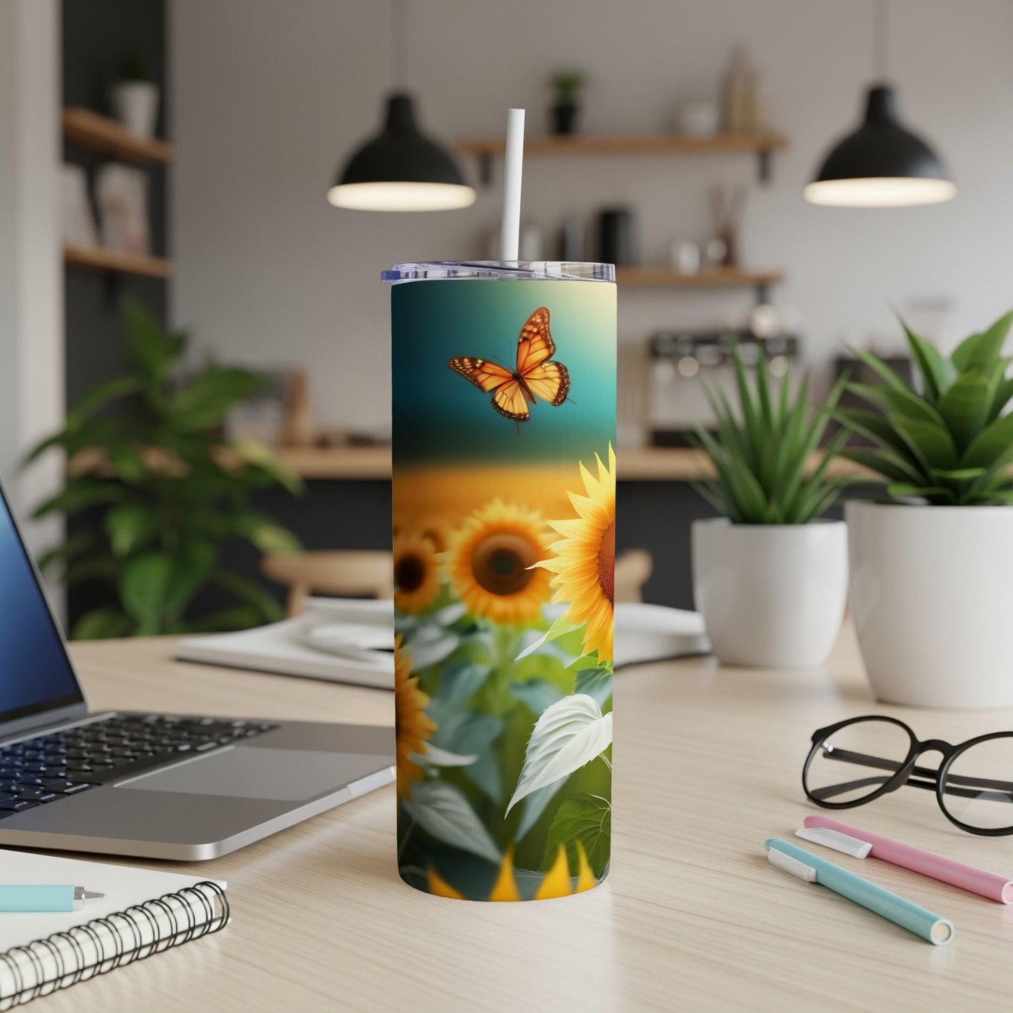 Sunflower and butterfly design on a white tumbler with straw, on a desk.