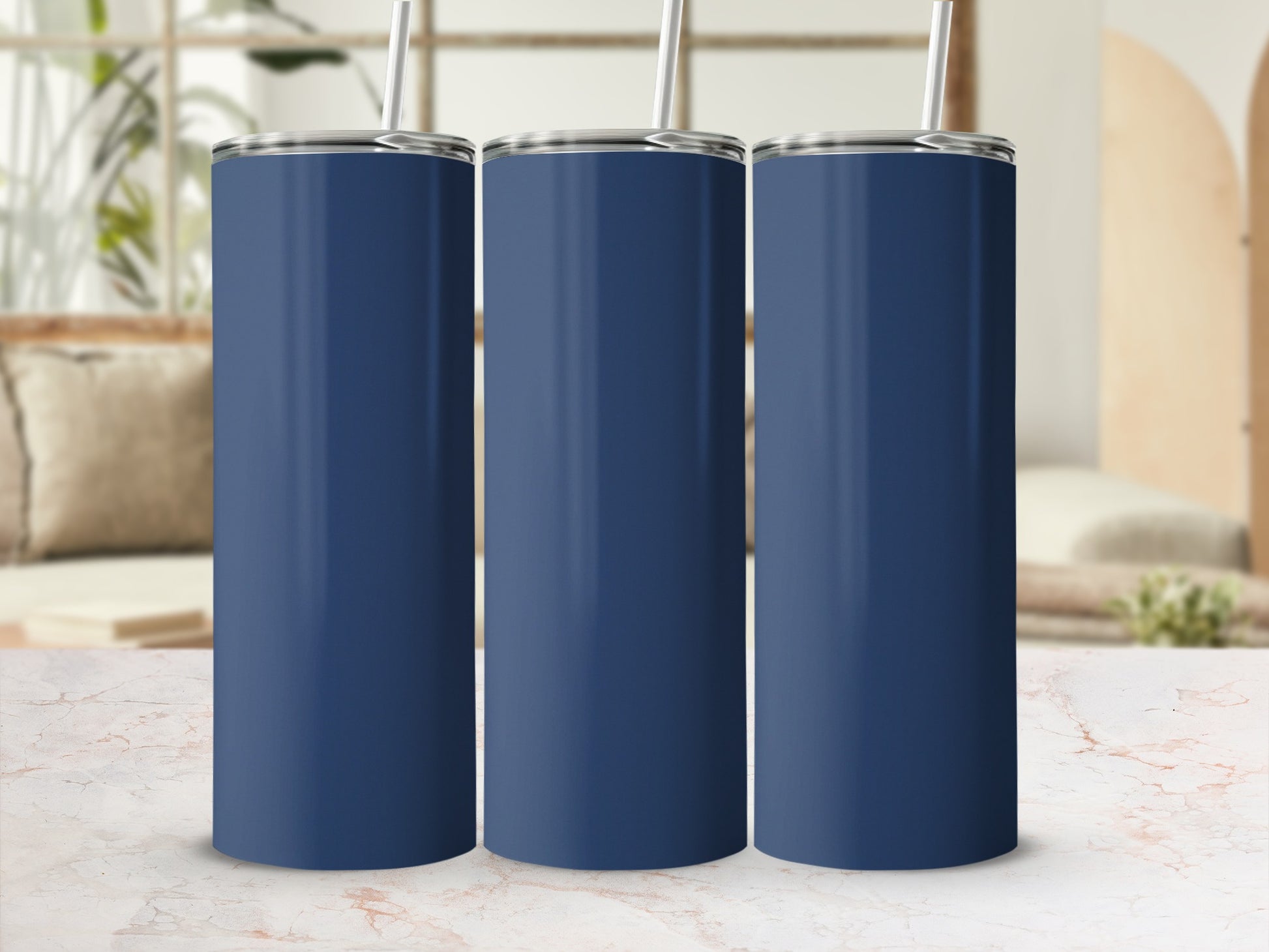 Three navy blue tumblers with straws in a row on a marble surface.