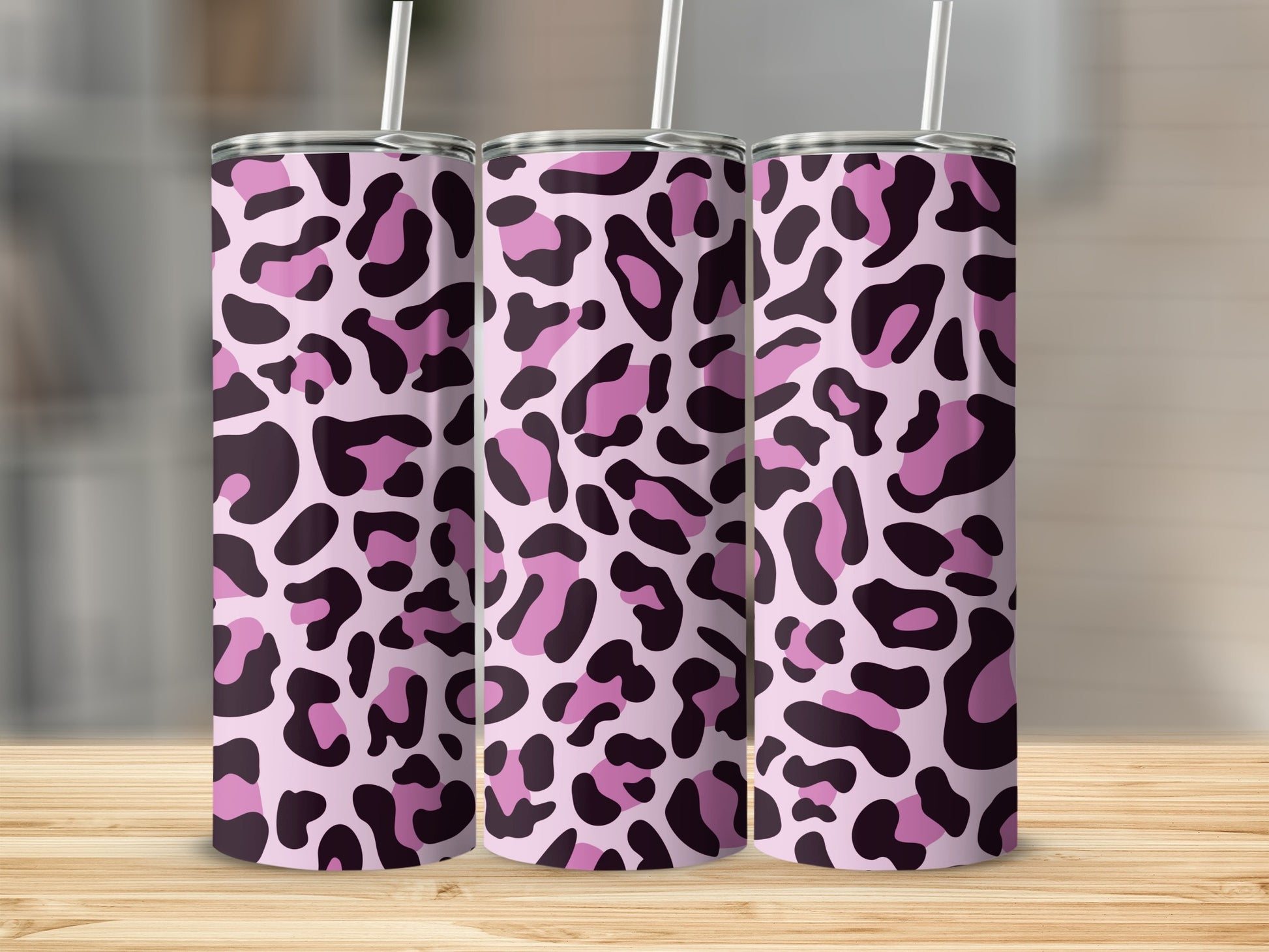 Three pink tumblers with a leopard print pattern on a wooden surface.