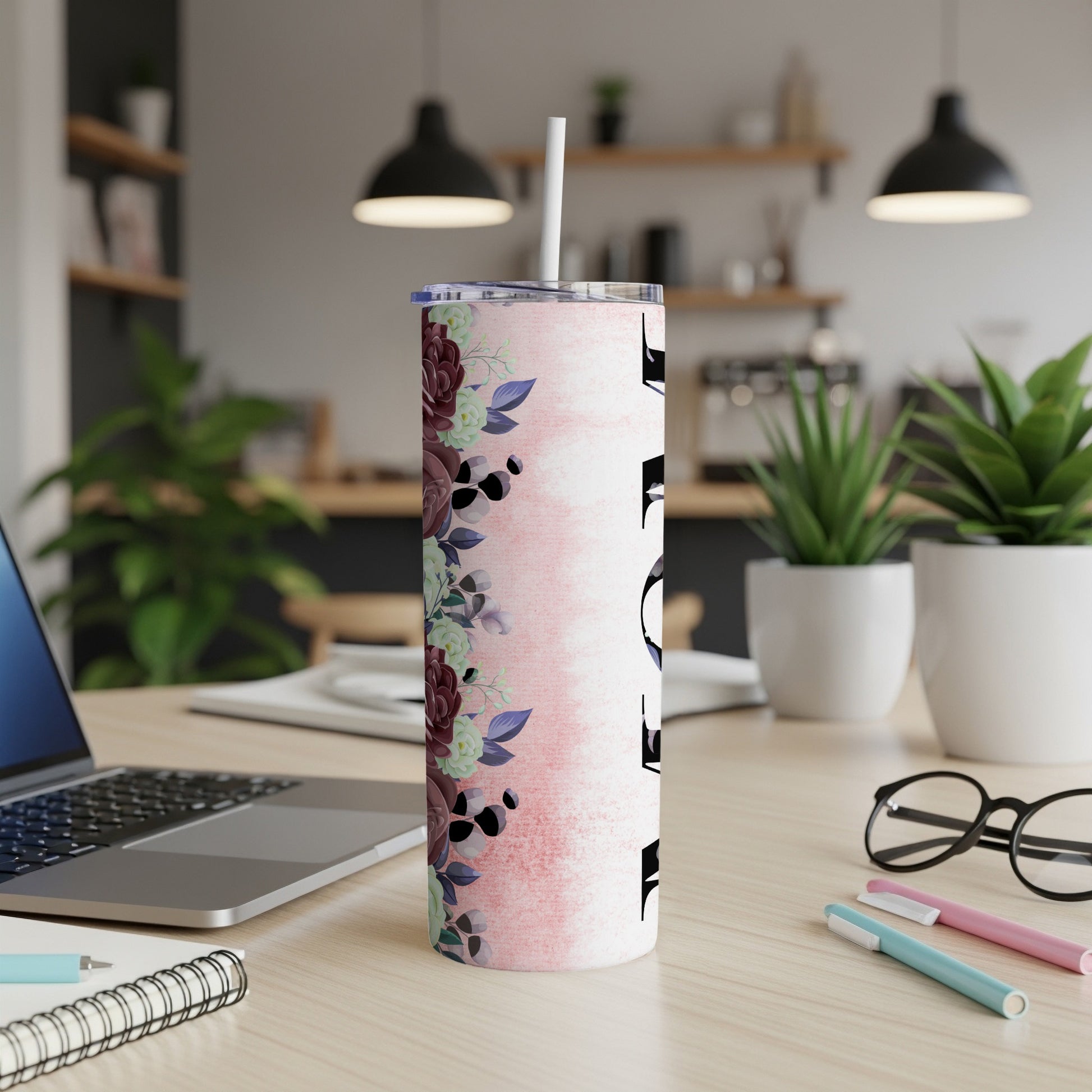 Pink floral tumbler with white lid and straw on a desk.