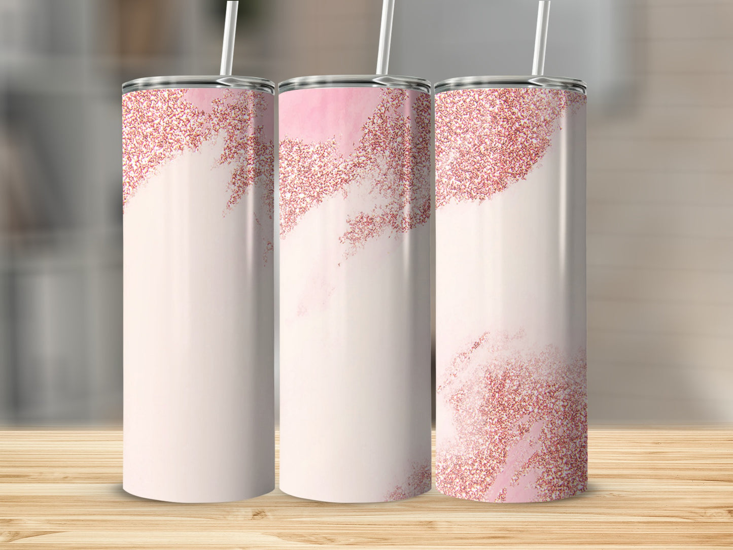 Three pink glitter tumblers with straws on a wooden surface.