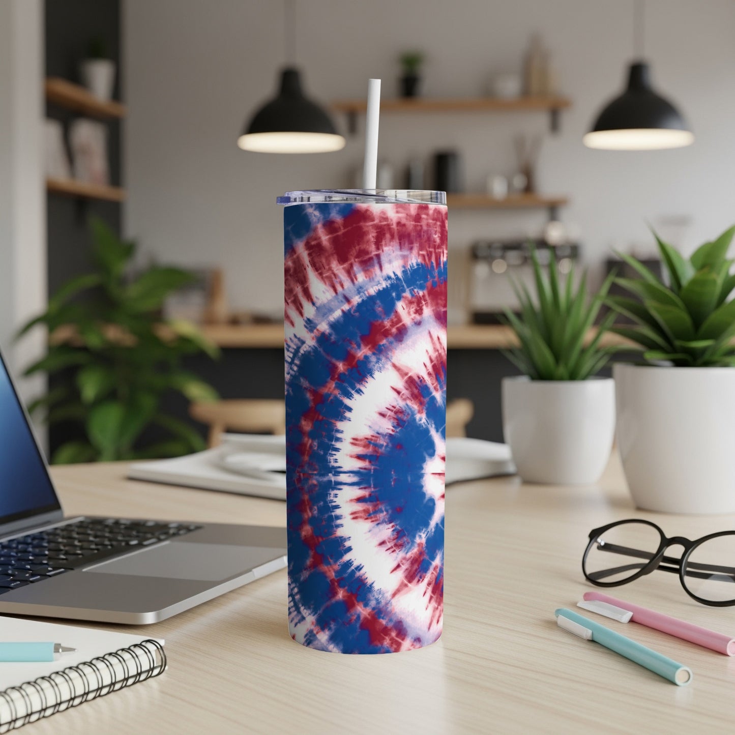 Red, white, and blue tie-dye tumbler with a straw on a wooden desk.