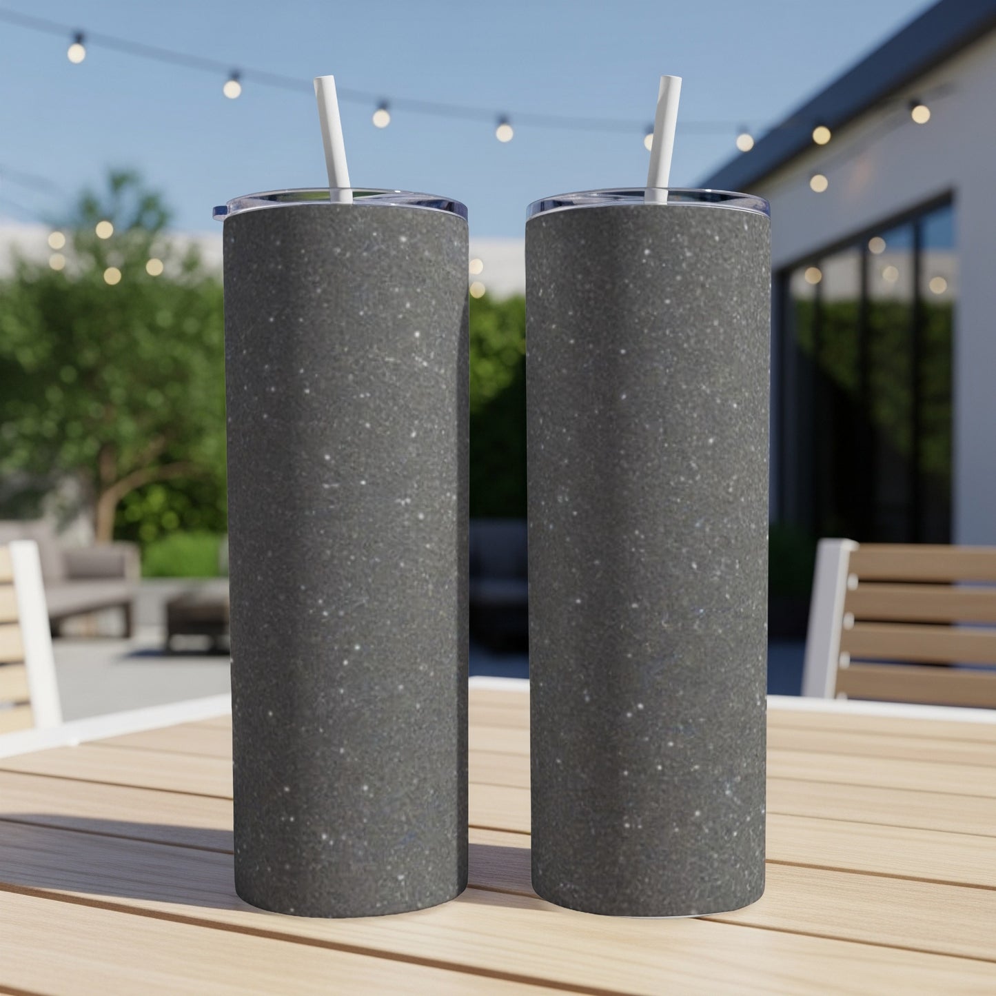 Two dark glitter-covered tumblers with straws on a wooden table.