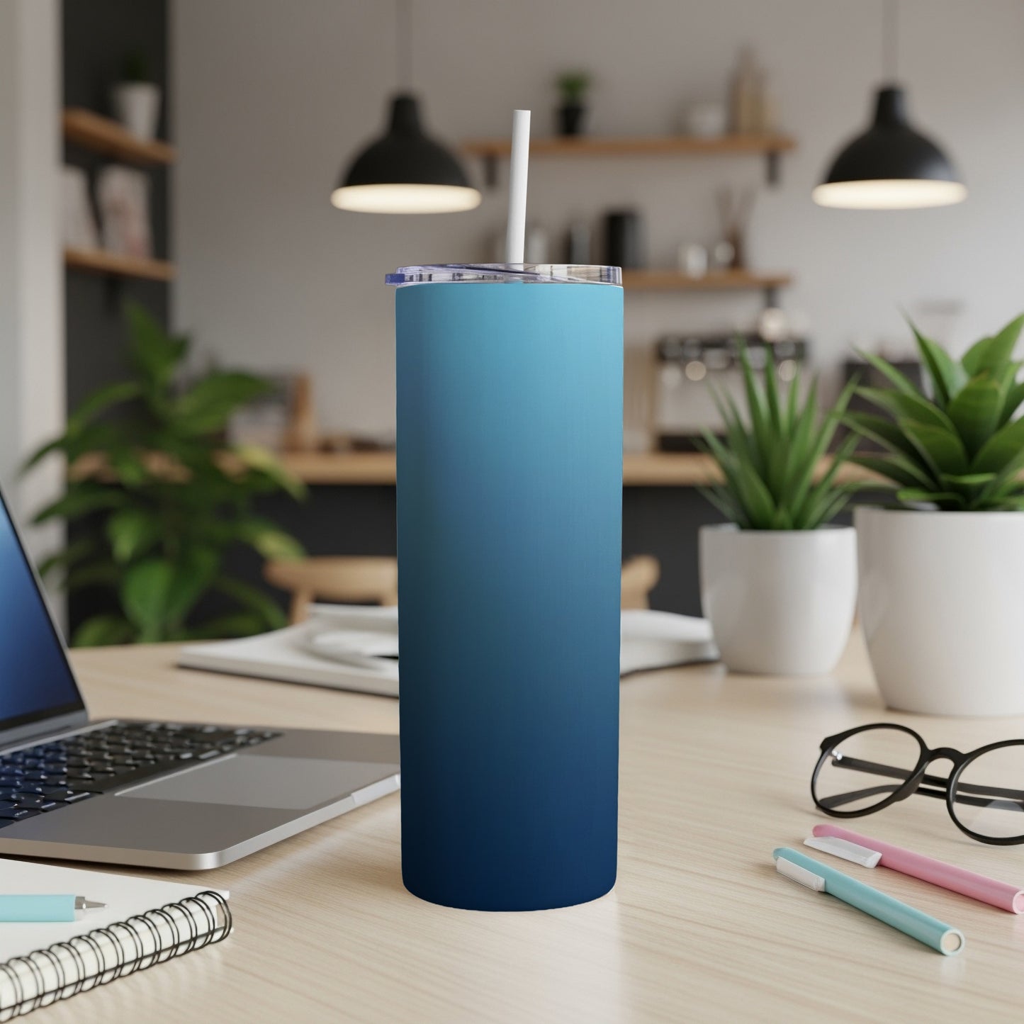 Blue gradient skinny tumbler with straw on a desk with laptop and plants.