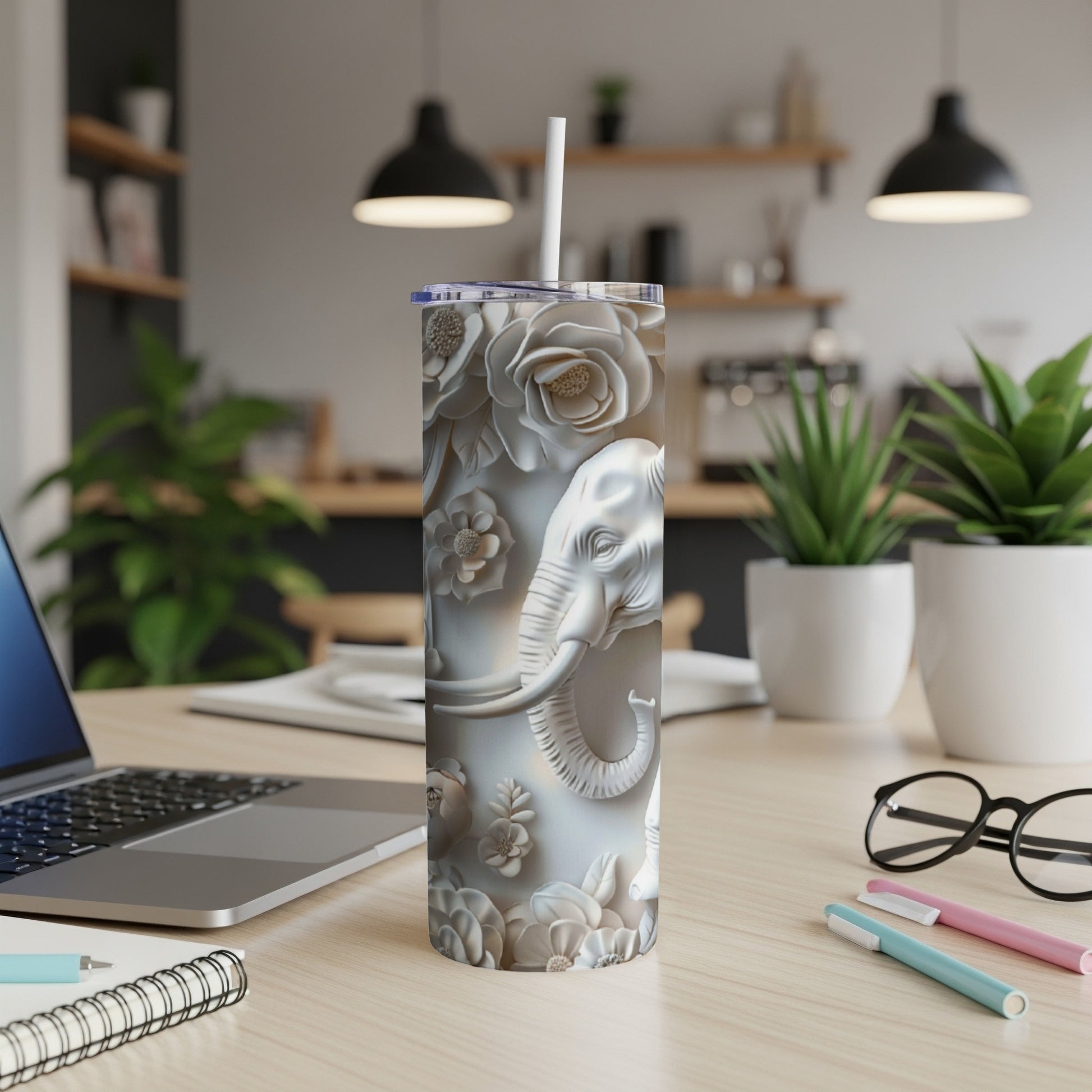 White tumbler with embossed elephant and floral pattern on desk.