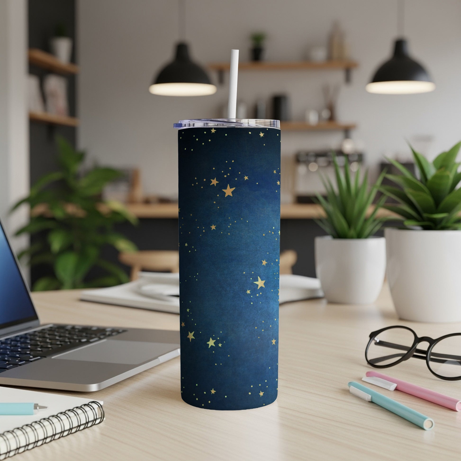 Dark blue tumbler with gold stars and a white straw on a desk.