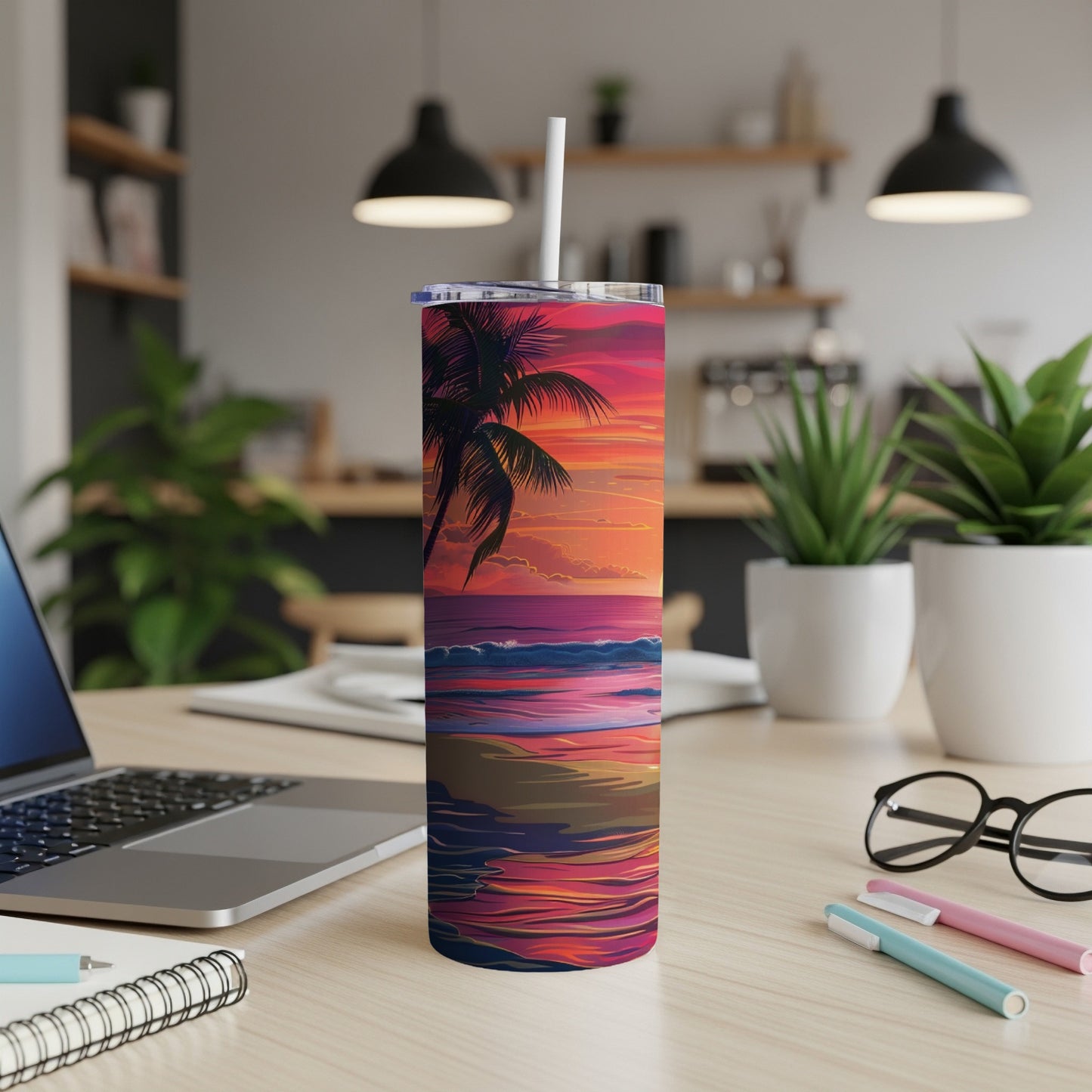 Tumbler with a tropical beach sunset design and straw, on a desk.