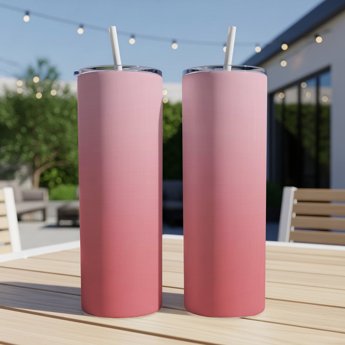 Two pink gradient tumblers with straws sit on a wooden table outdoors.